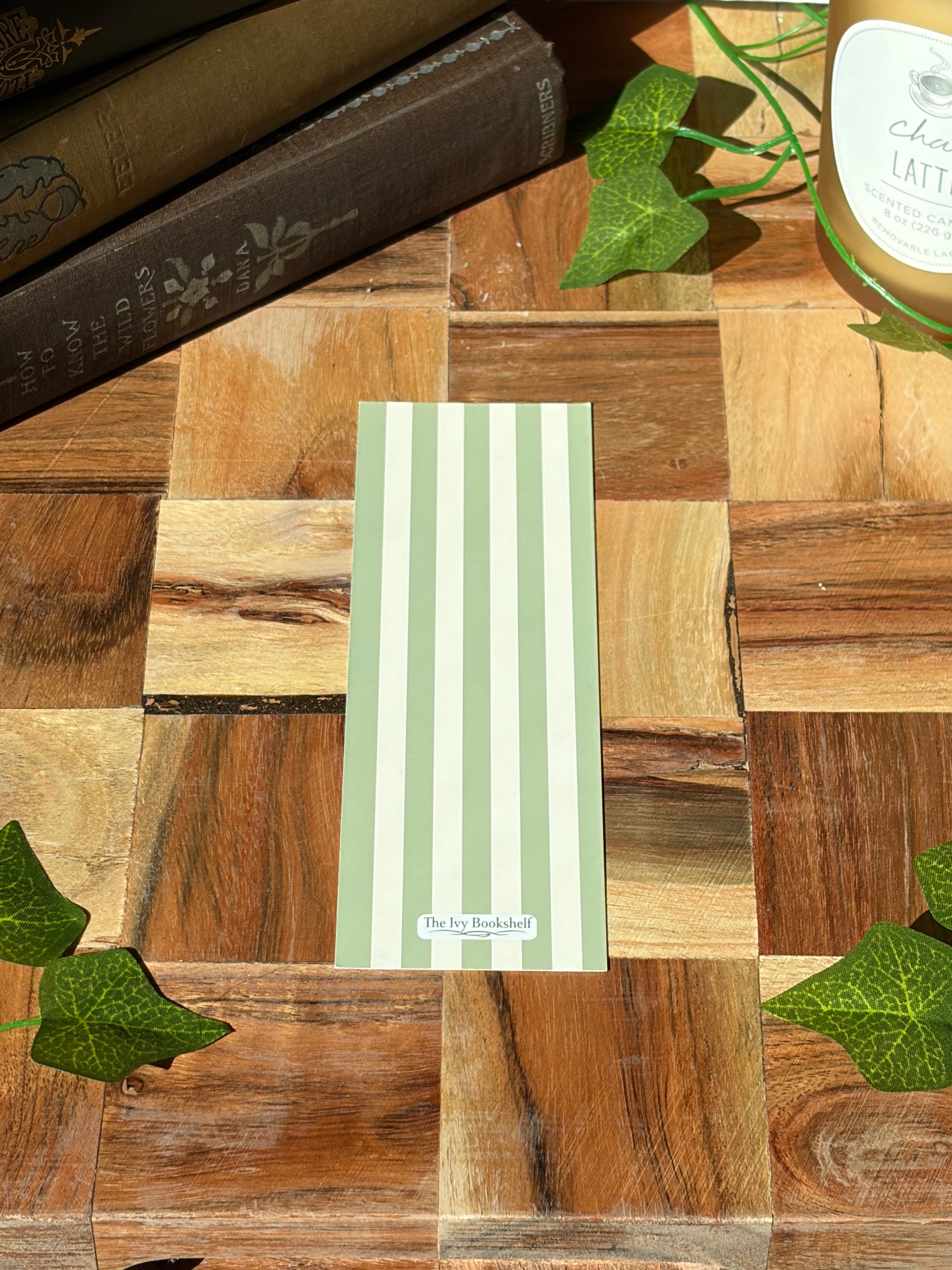 The back of the bookmark with green and white stripes, featuring a minimal logo at the bottom. The bookmark is sitting on a wooden background. 
