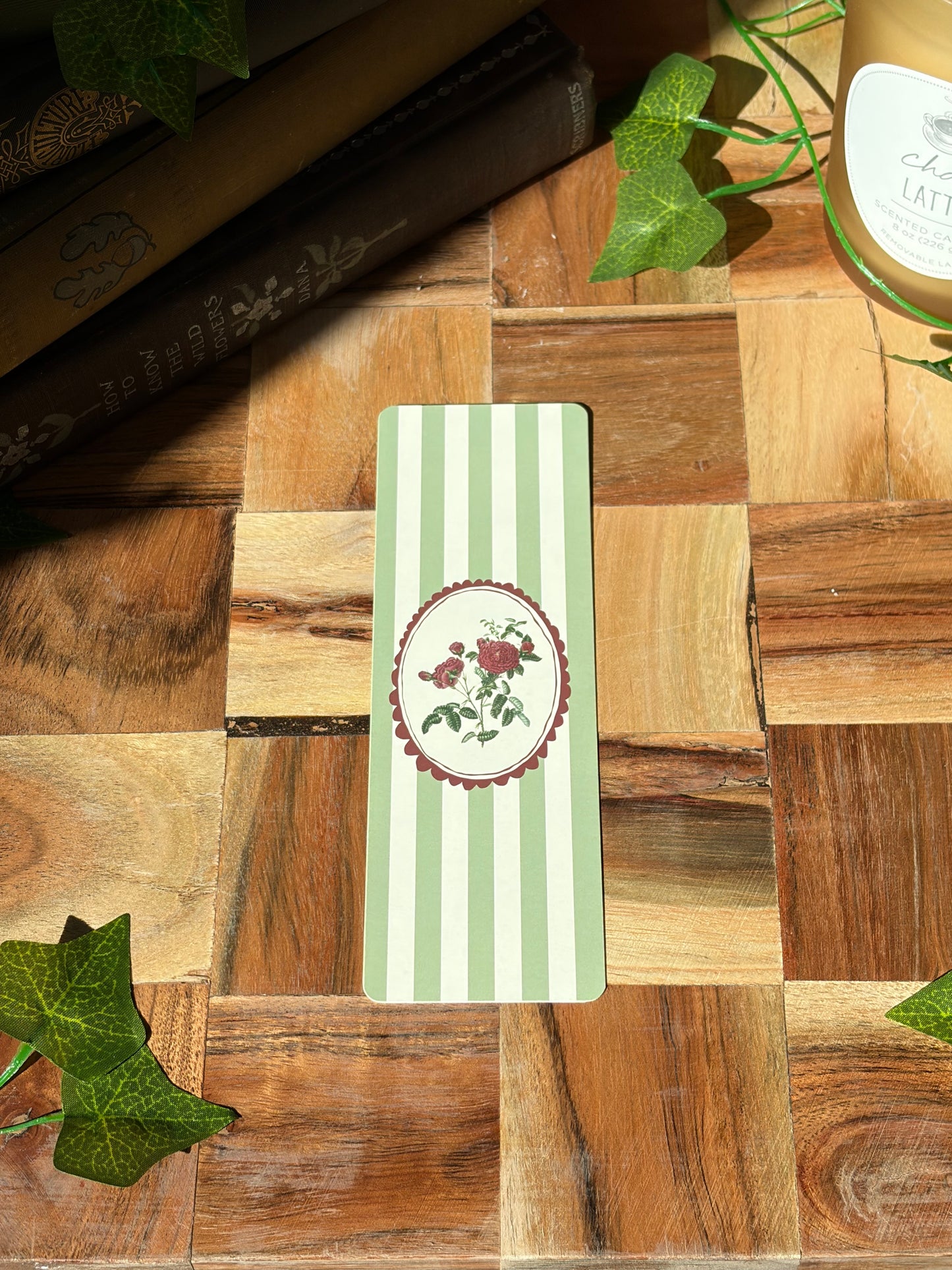 A green striped bookmark with a red round frame picturing red carnations in the center. Featuring an option with rounded corners. The bookmark is sitting on a wooden background. 