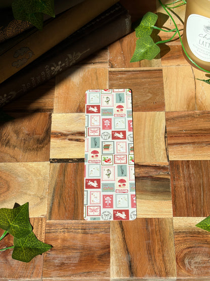 A bookmark with a variety of red, green, and cream stamp designs arranged in a pattern. Featuring an option for rounded edges. The bookmark is sitting on a wooden background. 