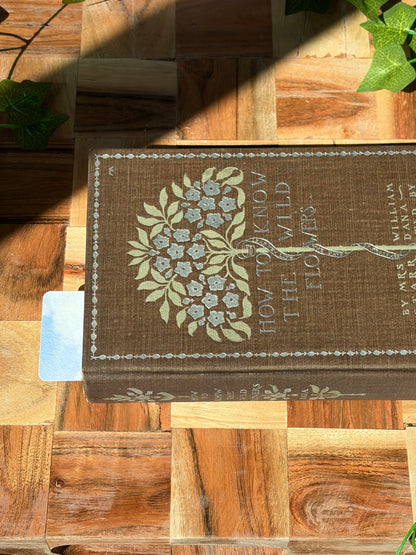 A watercolor landscape design sticking out the top of a closed book. The book is sitting on a wooden background.
